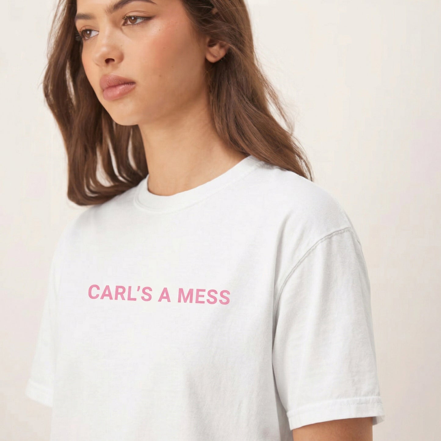 Person wearing a white t-shirt with 'CARL'S A MESS' text in pink on a plain background
