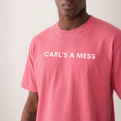Person wearing a pink t-shirt with 'CARL'S A MESS' text on a plain background